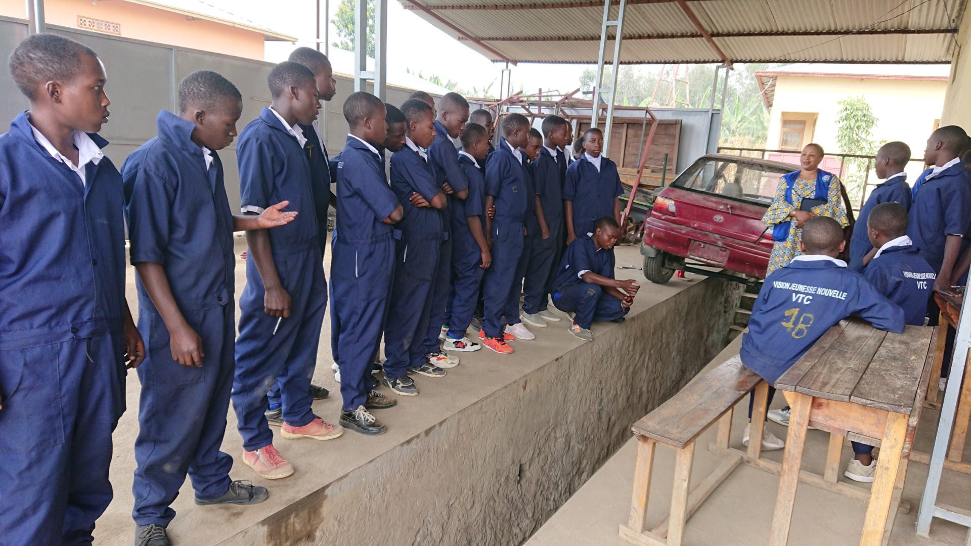 Vocational training students in workwear observing an automotive repair session at the VJN training centre